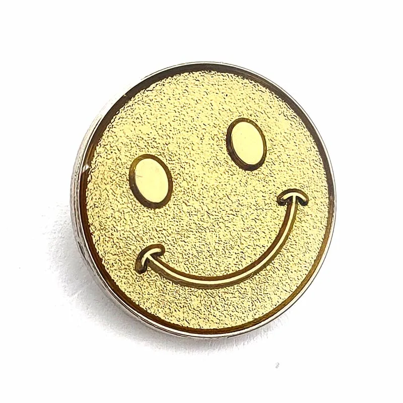 In French, the translation of "Gold Plated Sanded Metal Craft Souvenir Smiley Face Pin Badge" is "Insigne de broche en métal sablé plaqué or, souvenir d'artisanat avec un visage souriant".