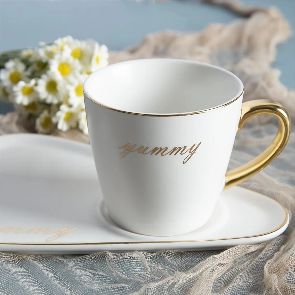 Taza de café de cerámica de color blanco y plato con el oro de la llanta y manejar
