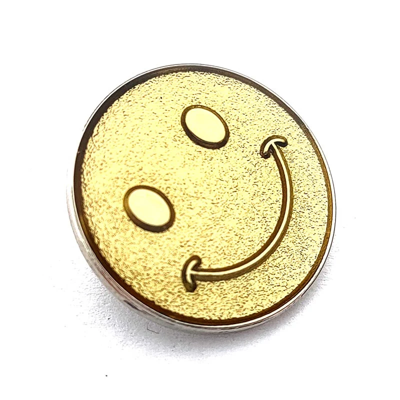 In French, the translation of "Gold Plated Sanded Metal Craft Souvenir Smiley Face Pin Badge" is "Insigne de broche en métal sablé plaqué or, souvenir d'artisanat avec un visage souriant".